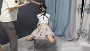 GG94-A barefoot Asian girl, bound to a chair, wearing a leather glove and a rubber gag, admires her bound appearance in front of a mirror.