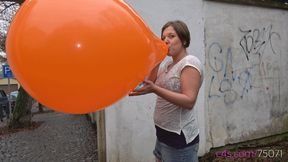 Simona inflates a giant orange balloon outside (4K quality)