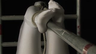 Encased girl in shiny zentai suit is tied to a metal pole and tries to escape