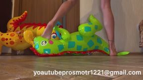 Nastya plays with her inflatable toys, two dinosaurs. She steps on them with her weight, tramples them, jumps on them, sits on their faces, and steps on their paws. Bare feet, foot fetish, inflatable