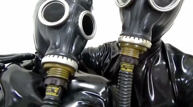 Latex-clad couple explores breathplay with gas masks in a stark white room