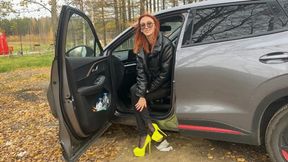 A girl in very high-heeled shoes is playing with a car in the woods, she really likes to pedal and play with shoes