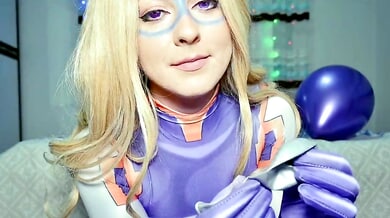 Blonde in purple latex superheroine costume plays with a silver balloon on a patterned bed