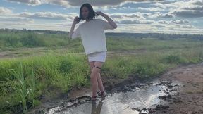 A girl in beautiful sexy high-heeled shoes walks through the stinking mud