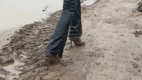 A girl in shiny high-heeled shoes walks through a mud field and gets her shoes and pants dirty (short version)