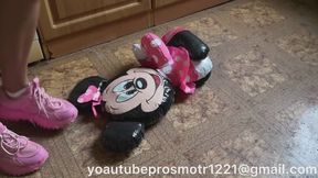 Nastya, wearing pink sneakers, tramples on an inflatable Mickey Mouse toy, and also tramples on it barefoot, steps on it with all her weight, crushes it, stands on it, and presses it.