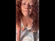 Curly haired girl smiles while showing off her tattooed arm and cleavage