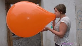 Simona inflates a giant orange balloon outside (HD quality)