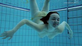 Brunette lady takes off her swimsuit while swimming underwater