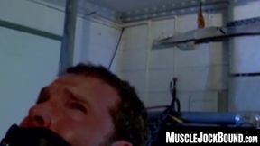 Muscular man silenced with a ball gag while being heavily chained and mercilessly tormented in a dark dungeon