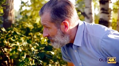 Young brunette with glasses gives deep throat to older bearded man in sunlit meadow