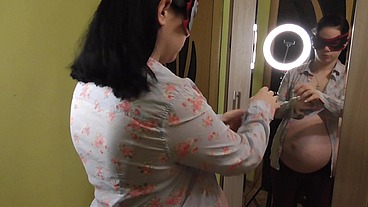Pregnant Anna trying on dresses in front of a mirror