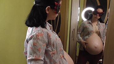 Pregnant Anna trying on dresses in front of a mirror