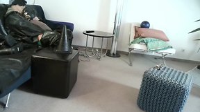 Latex masked person enjoys sitting on giant sextoy plug