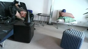 Latex masked person enjoys sitting on giant sextoy plug