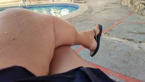 A beautiful woman in front of a pool leaves flip-flops hanging from her feet (1)