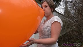 Simona inflates a giant orange balloon outside (MOBILE quality)