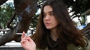 Young brunette is taking an unhurried stroll with allwhite 120mm cigarette