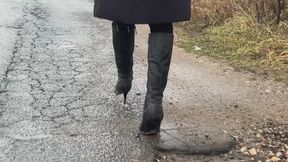 A girl in high-heeled leather boots walks through mud in bad weather, slips on mud and gets her boots dirty