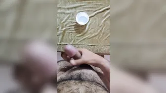 Hairy young stud strokes big cock and collects thick cum in container